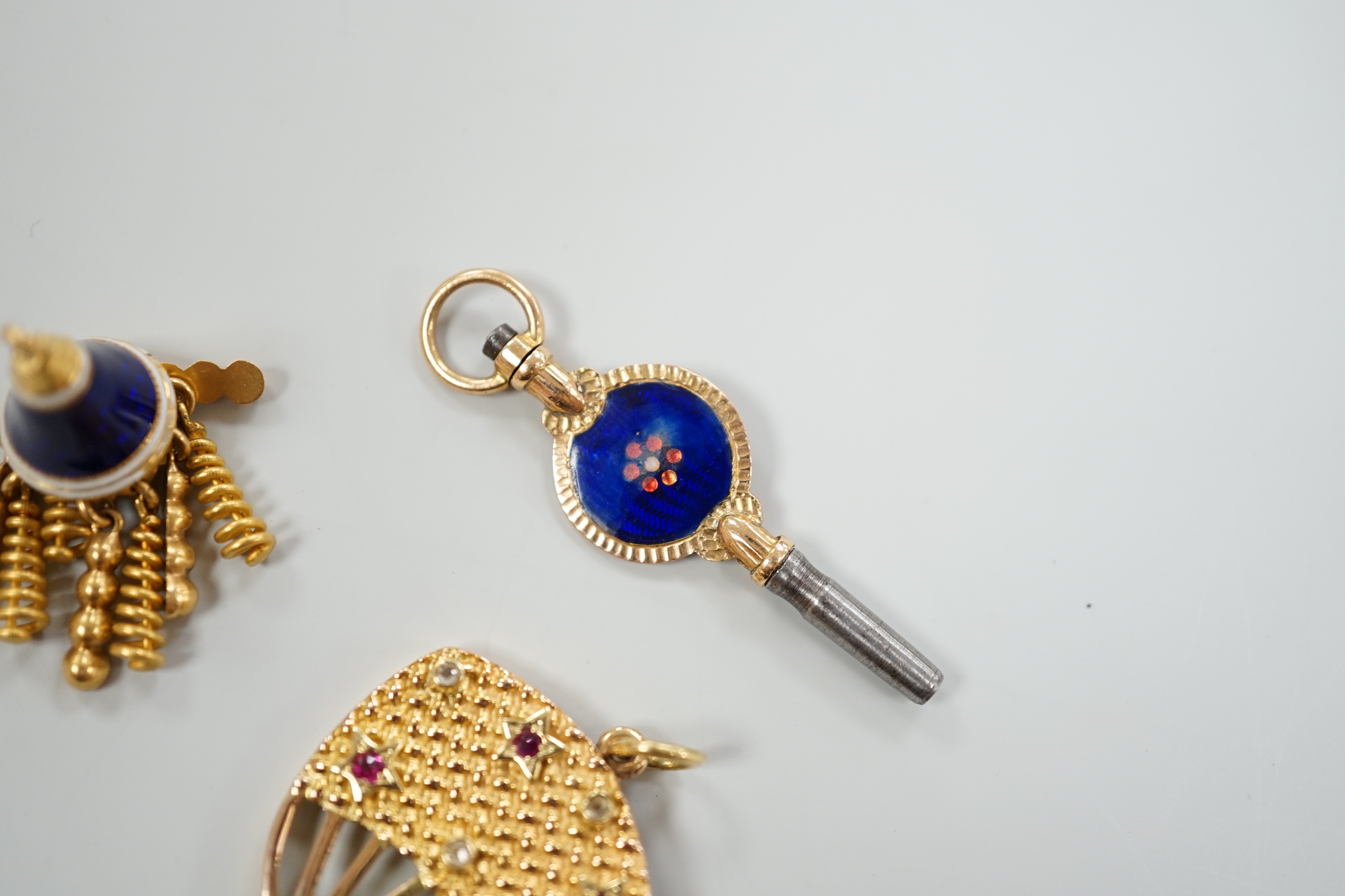 An early 20th century yellow metal (stamped 15), ruby and diamond set watch key, 39mm, together with a three colour enamelled watch key and an enamelled tassel charm.